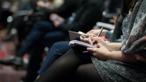 A row of conference attendees writing in notebooks