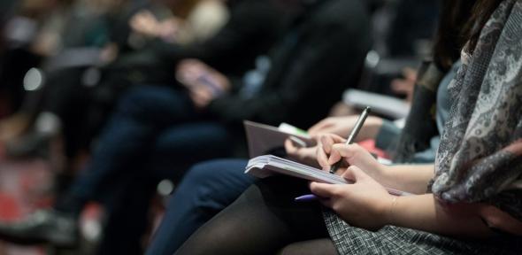 A row of conference attendees writing in notebooks